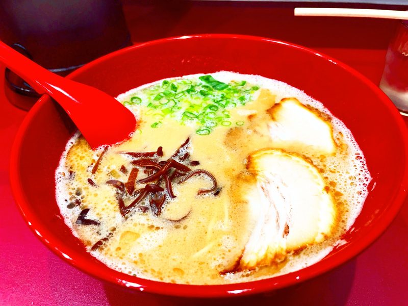 赤いどんぶりに入った、チャーシューとネギをのせた豚骨ラーメン
